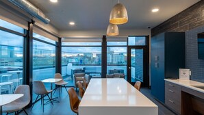 A modern kitchen with a large island, dark cabinetry, and a view of the city through large windows. - Modern Studio Apt with Rooftop, Gym, and Parking (Milwaukee)