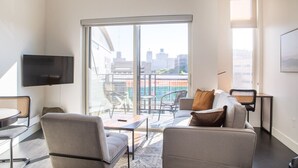 A modern living room with a large sliding glass door leading to a balcony, a flat-screen TV mounted on the wall, and a seating area with a sofa and chairs. - Modern Studio Apt with Rooftop, Gym, and Parking (Milwaukee)