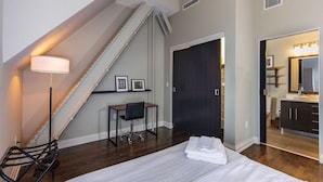 Un dormitorio con cama, escritorio, silla, lámpara y una escalera.