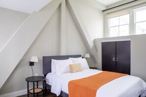 A bedroom with a bed, bedside lamps, a small round table, a wardrobe, and a sloped ceiling. - Downtown Luxury 1BR Loft · Walkable · Sleeps 4 (Milwaukee)