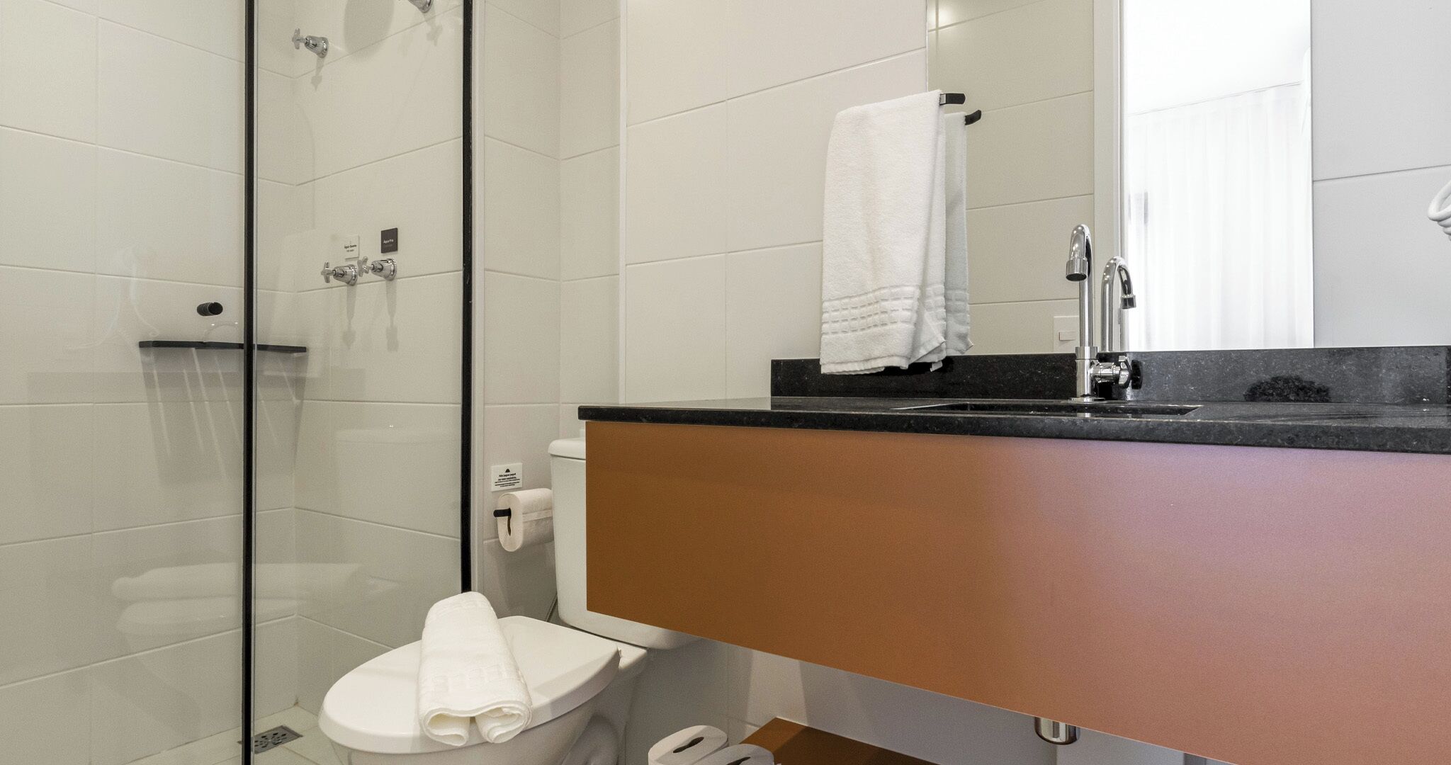 A modern bathroom with a glass shower enclosure, a toilet, and a sink with a towel hanging on the wall.