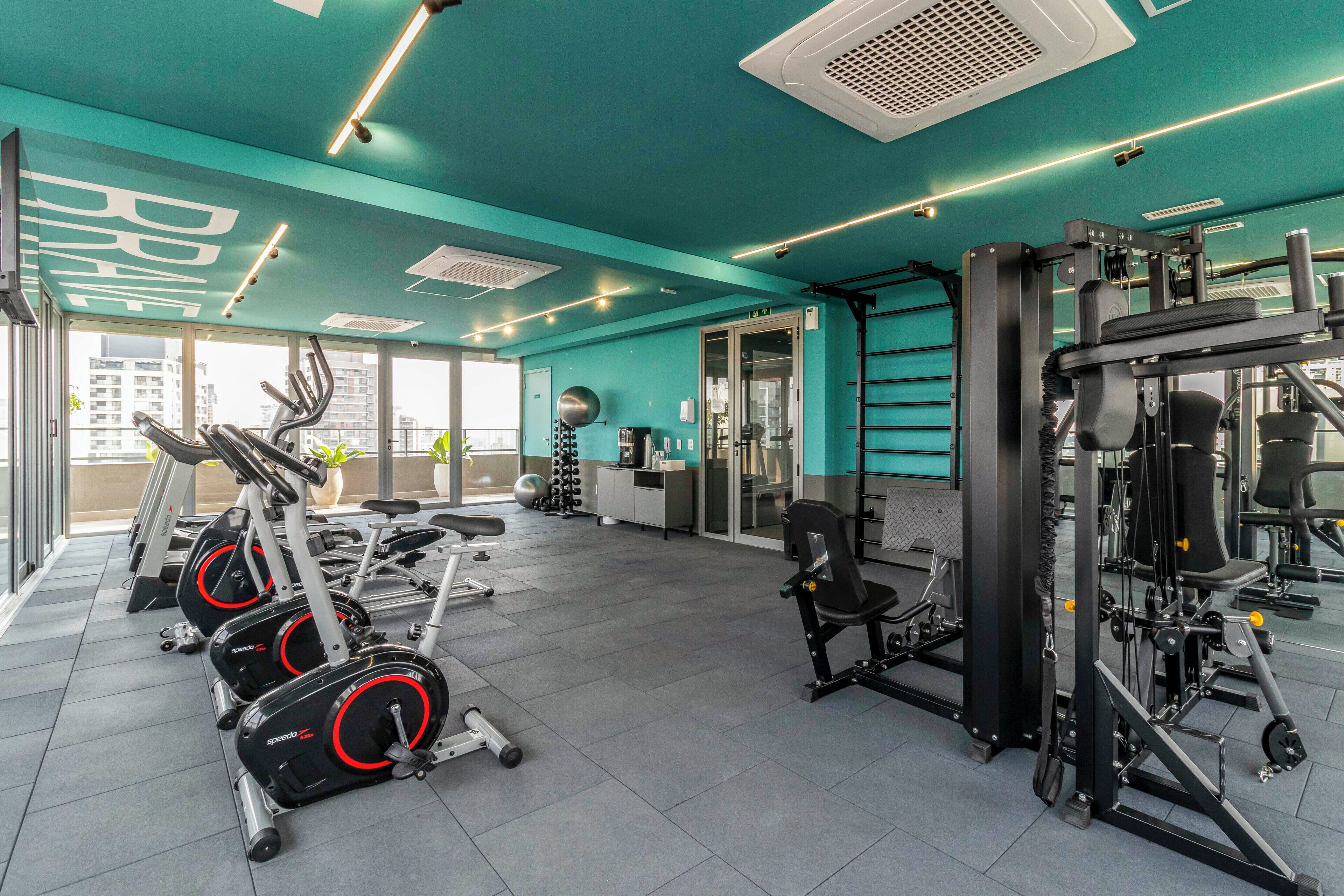 A gym with exercise equipment, a large window, and a teal-colored ceiling.
