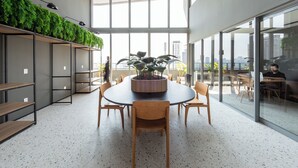 A modern meeting room with a round table, chairs, a potted plant, and a city view through large windows. - Charlie Wonder Brooklin (São Paulo)