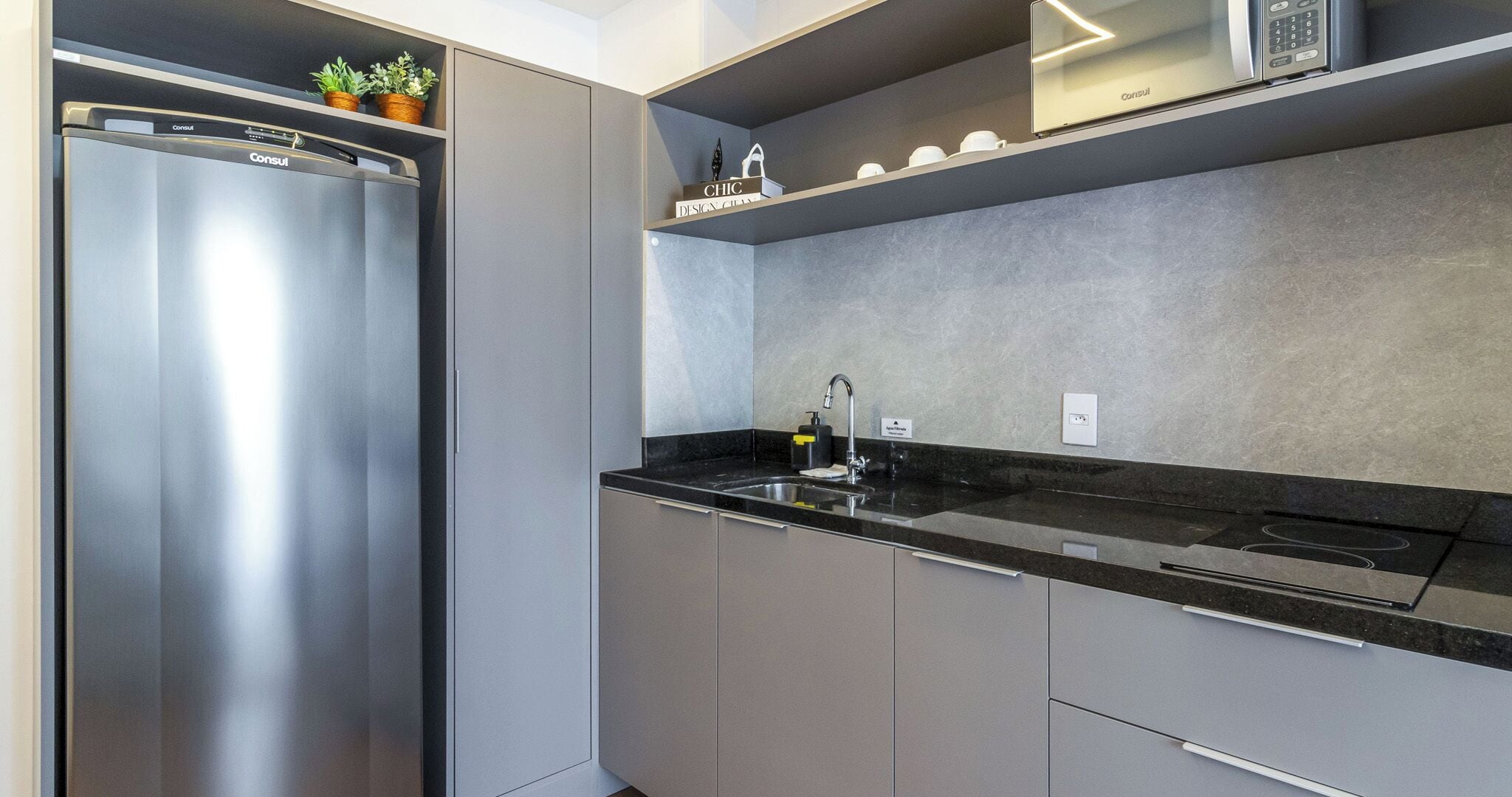 A modern kitchen with a stainless steel refrigerator, a black countertop, and grey cabinets.