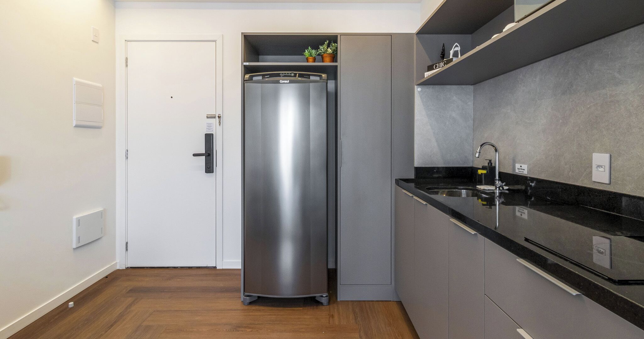 Eine kompakte Küche mit einem Edelstahl-Kühlschrank, einer schwarzen Arbeitsplatte und einer integrierten Spüle.