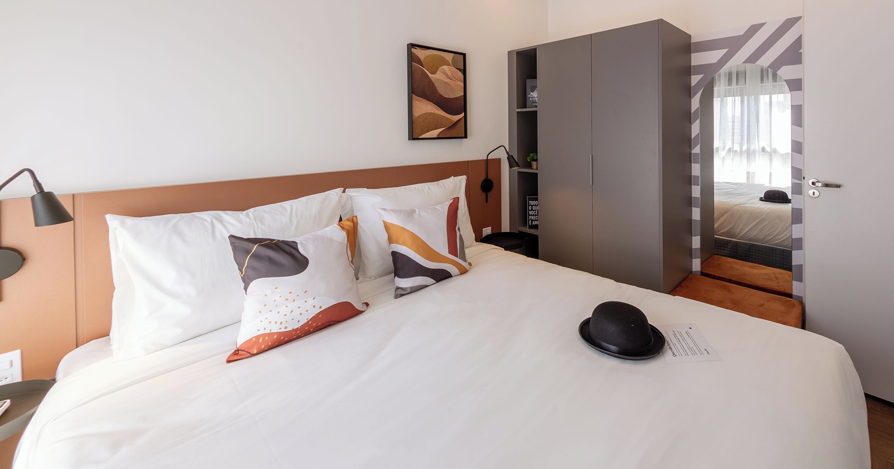 Una habitación de hotel con una cama bien hecha, un armario y un escritorio con lámpara.