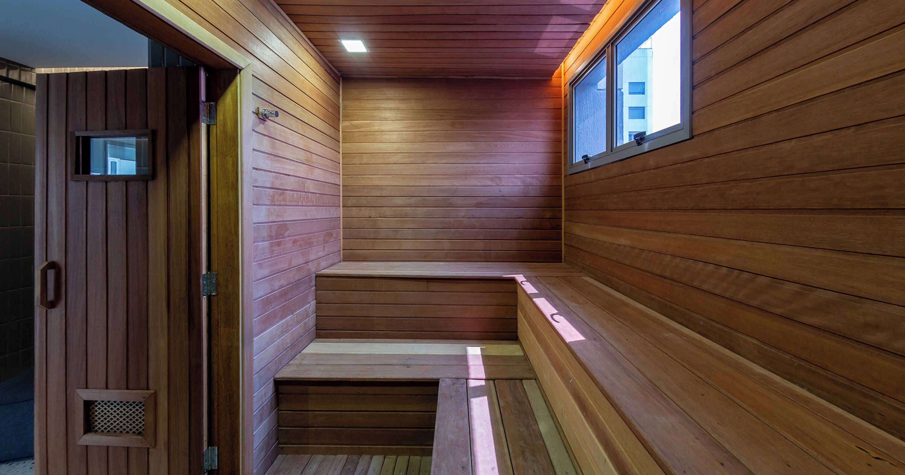 A wooden sauna with a bench, a small window, and a door.