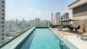 A rooftop pool with a city view, a seating area with tables and chairs, and a glass railing. - Charlie Wonder Brooklin (São Paulo)