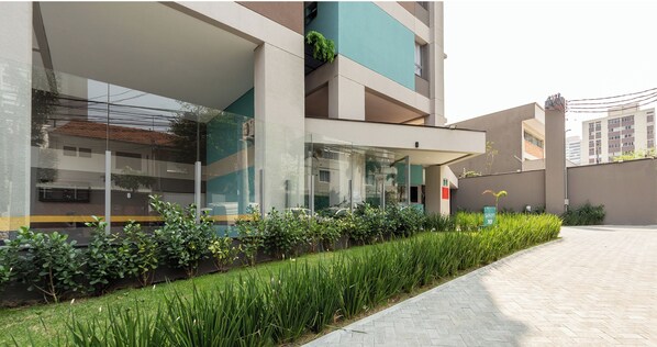 Un edificio moderno con grandes ventanales, fachada de vidrio y un área ajardinada con plantas verdes.