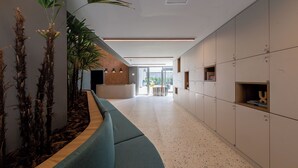 A modern reception area with a curved bench, potted plants, and a reception desk. - Charlie Wonder Brooklin (São Paulo)