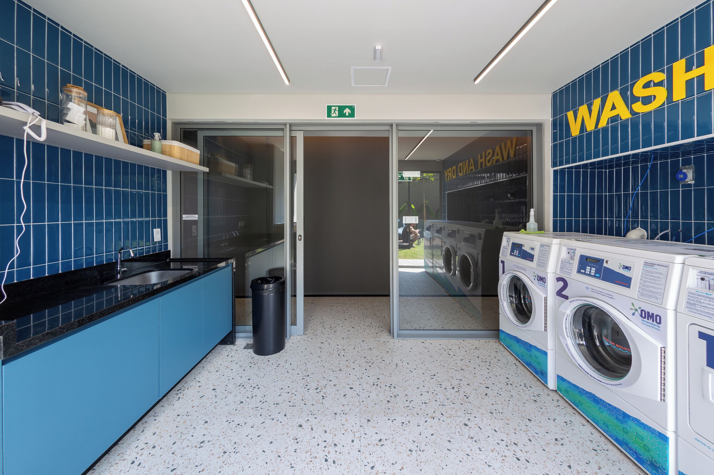 A modern laundry room with blue tiled walls, a sink, and two washing machines.