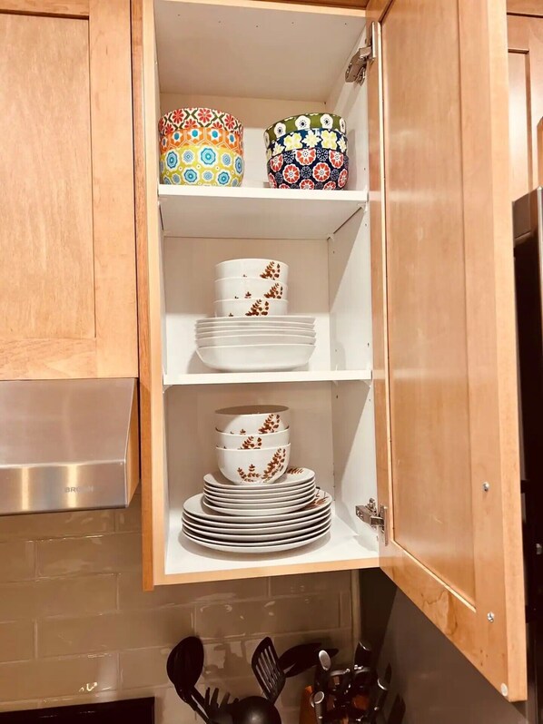 A kitchen cabinet with shelves holding various dishes and utensils.