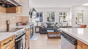 A modern kitchen with a built-in oven and stove, a dining area with a sofa and coffee table, and a view of a snowy landscape through large windows.