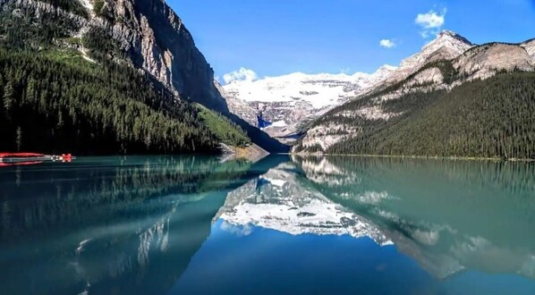 A calm lake with a mountain backdrop, clear reflections, and a red boat on the left.