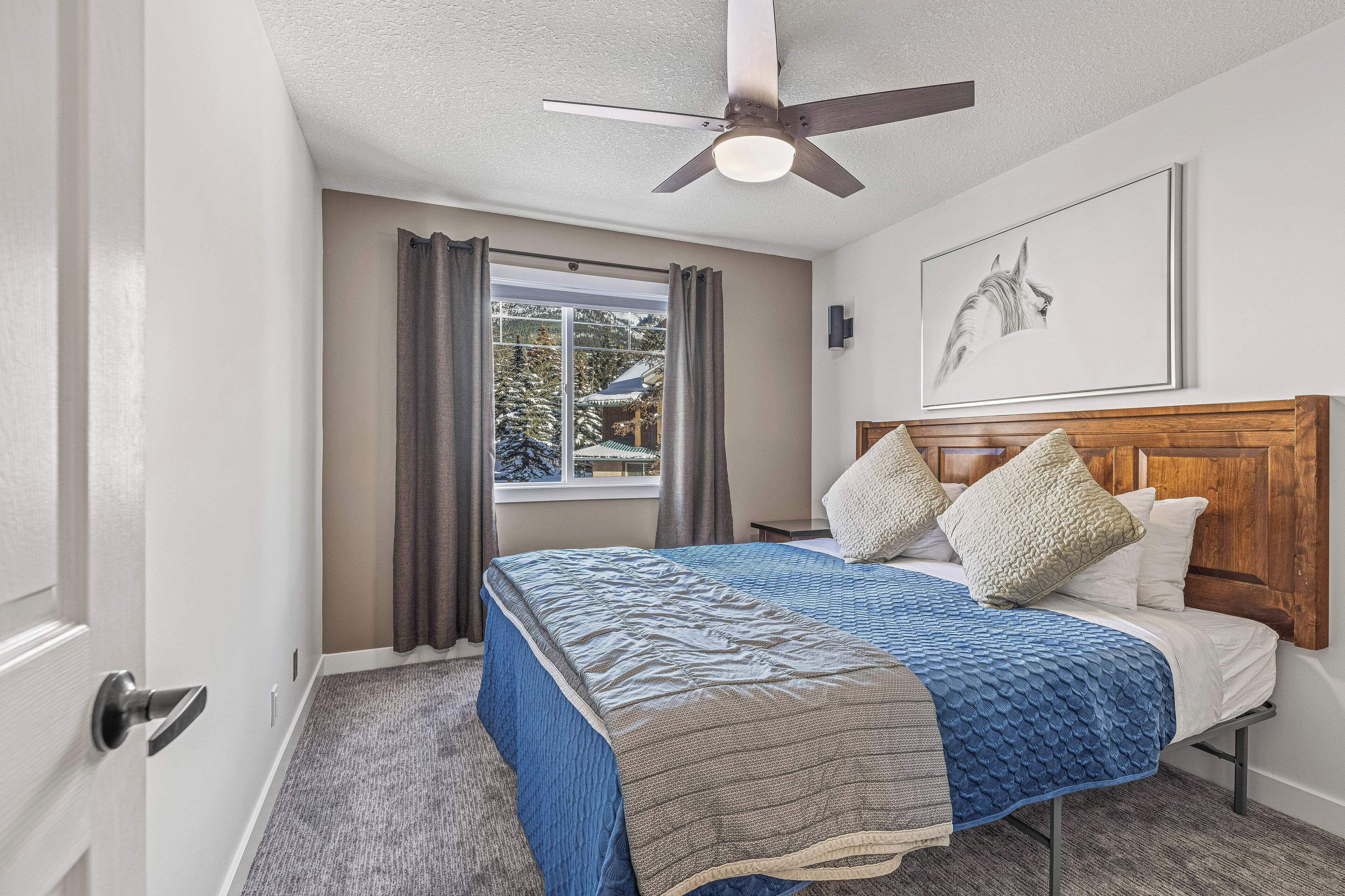 A bedroom with a bed, a ceiling fan, a window with curtains, and a framed picture on the wall.