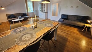 A modern loft with a dining area featuring a wooden table and chairs, a sofa, and a kitchen in the background.
