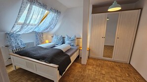 A bedroom with a bed, a bedside table, a lamp, a wardrobe, and a window with curtains.