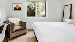 Ein Schlafzimmer mit einem großen Bett, einem Sessel, einem Schreibtisch und einem Fenster mit Blick auf Bäume.