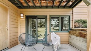 Eine überdachte Terrasse mit zwei schwarzen Stuhlgestellen, einem Tisch mit weißer Tischdecke und einem Schuhpaar auf dem Boden.