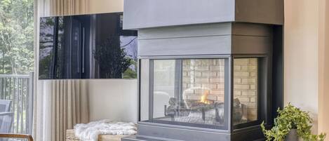 Una chimenea moderna con recinto de vidrio, un banco de madera y una planta en maceta.