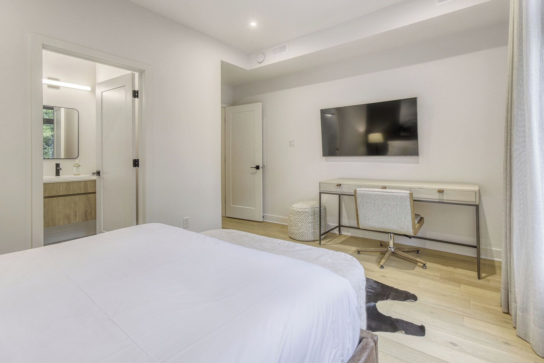 Ein modernes Schlafzimmer mit einem großen Bett, einem Schreibtisch mit Stuhl, einem Spiegel und einem Fernseher an der Wand.