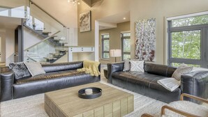 A modern living room with leather sofas, a wooden coffee table, and a staircase with glass railings. - 201 Verbier Building 7 (Mont-Tremblant)
