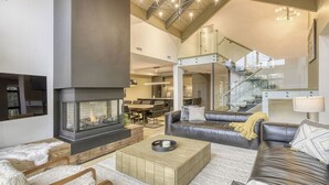 A spacious living room with a fireplace, leather sofas, a coffee table, and a staircase leading to an upper level. - 201 Verbier Building 7 (Mont-Tremblant)