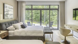 A modern bedroom with a large bed, a desk, and a view of a forest through floor-to-ceiling windows. - 201 Verbier Building 7 (Mont-Tremblant)