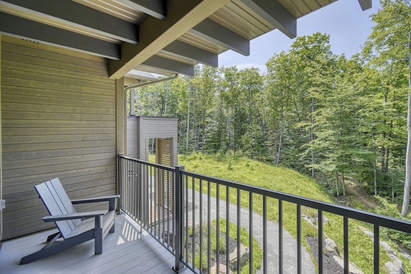 A balcony with a wooden floor, a metal railing, and a view of a forested area. - 201 Verbier Building 7 (Mont-Tremblant)