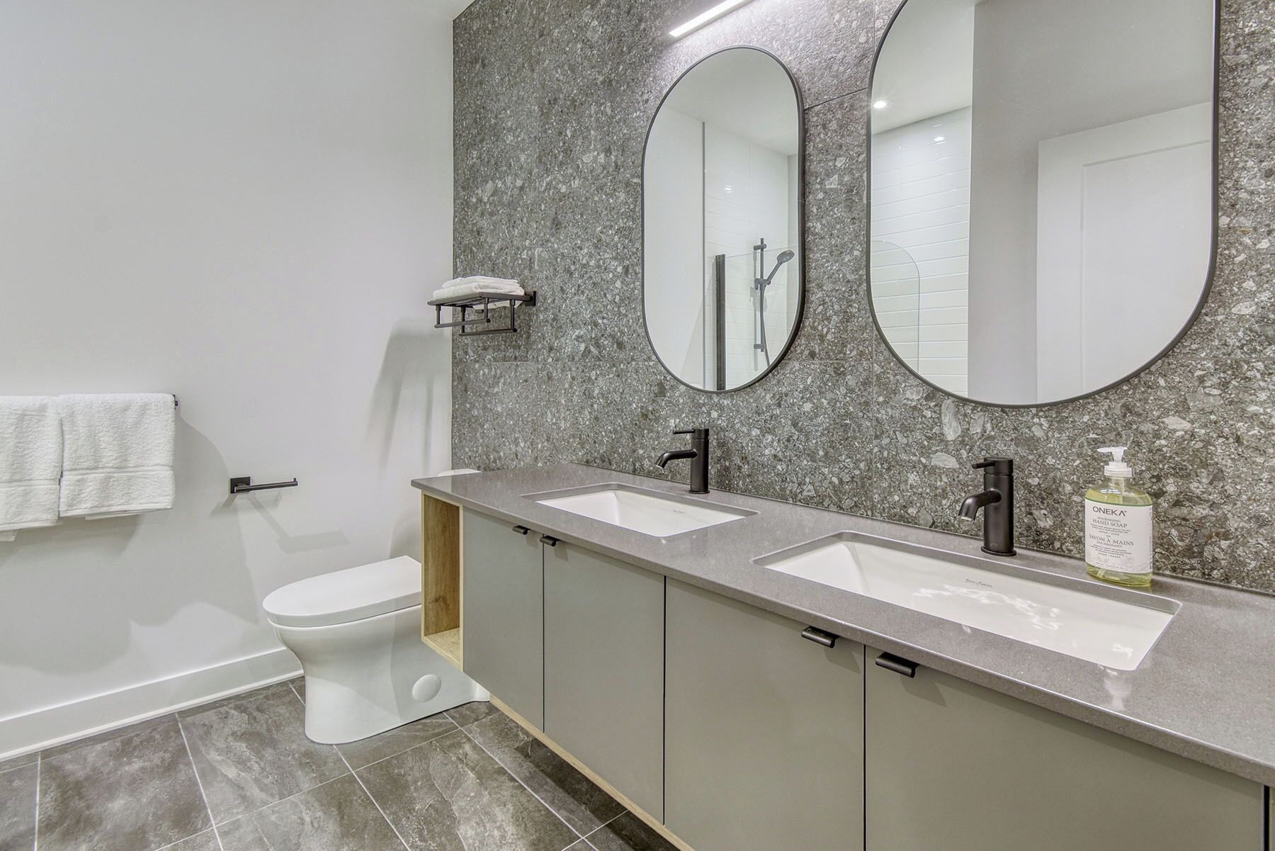 A modern bathroom with two sinks, a toilet, and a large mirror.