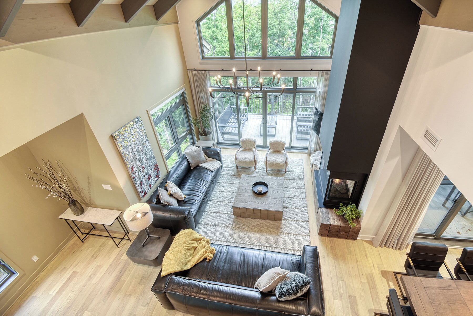 A modern living room with a black leather sofa, a coffee table, and a view of a deck through large windows.