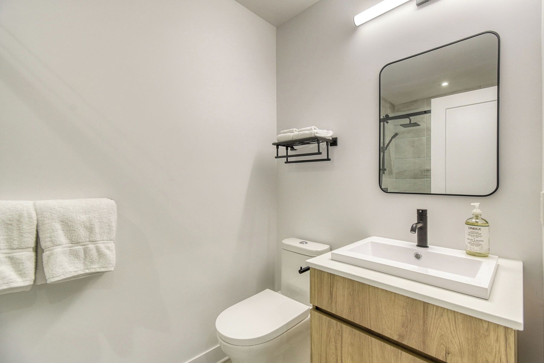 Un baño moderno con inodoro blanco, lavabo con espejo encima y toallero en la pared.