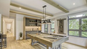 A modern living room with a pool table, a kitchen area, and large windows offering a view of the outdoors. - 201 Verbier Building 7 (Mont-Tremblant)