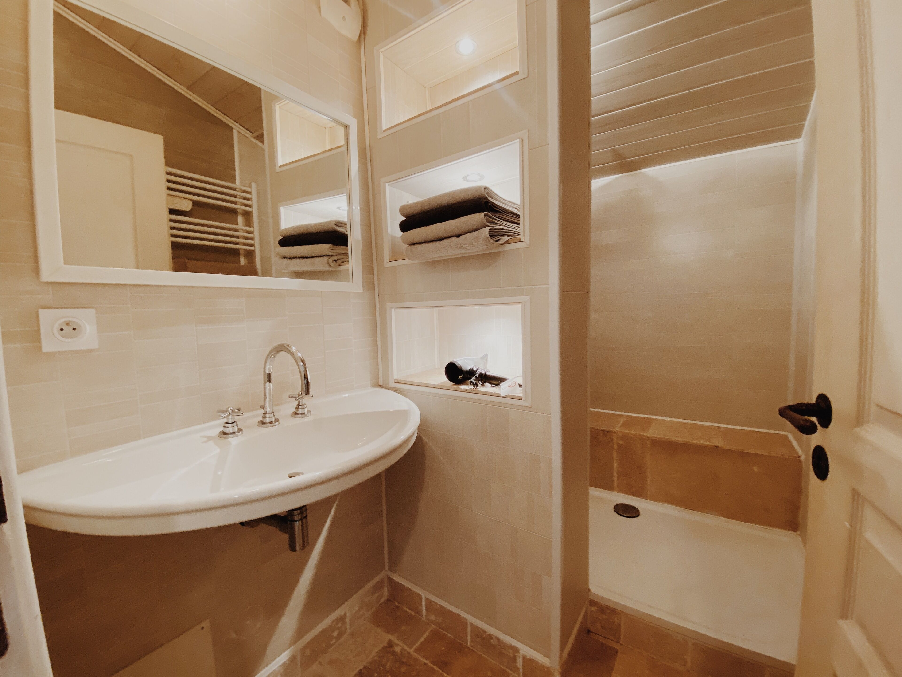 Een badkamer met een wastafel, spiegel, handdoekhouders en een douchehoek.