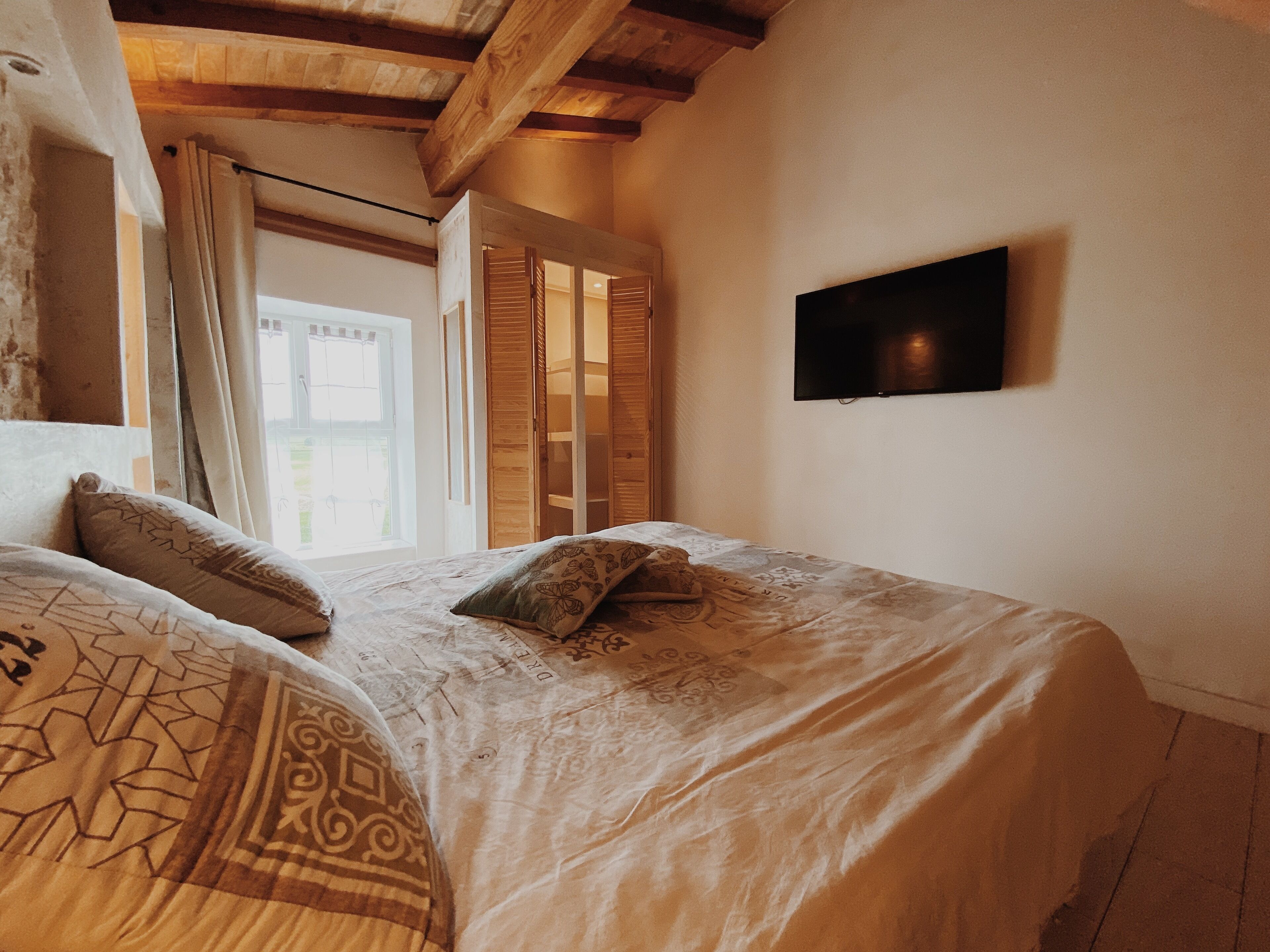 A bedroom with a bed, a TV, and a window with curtains.