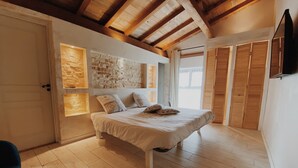 Un dormitorio con techo de madera, una cama con almohadas estampadas y una pared de piedra.