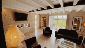 Amplia sala de estar con pared de piedra, televisor de pantalla plana, chimenea y un gran ventanal que da a un jardín.