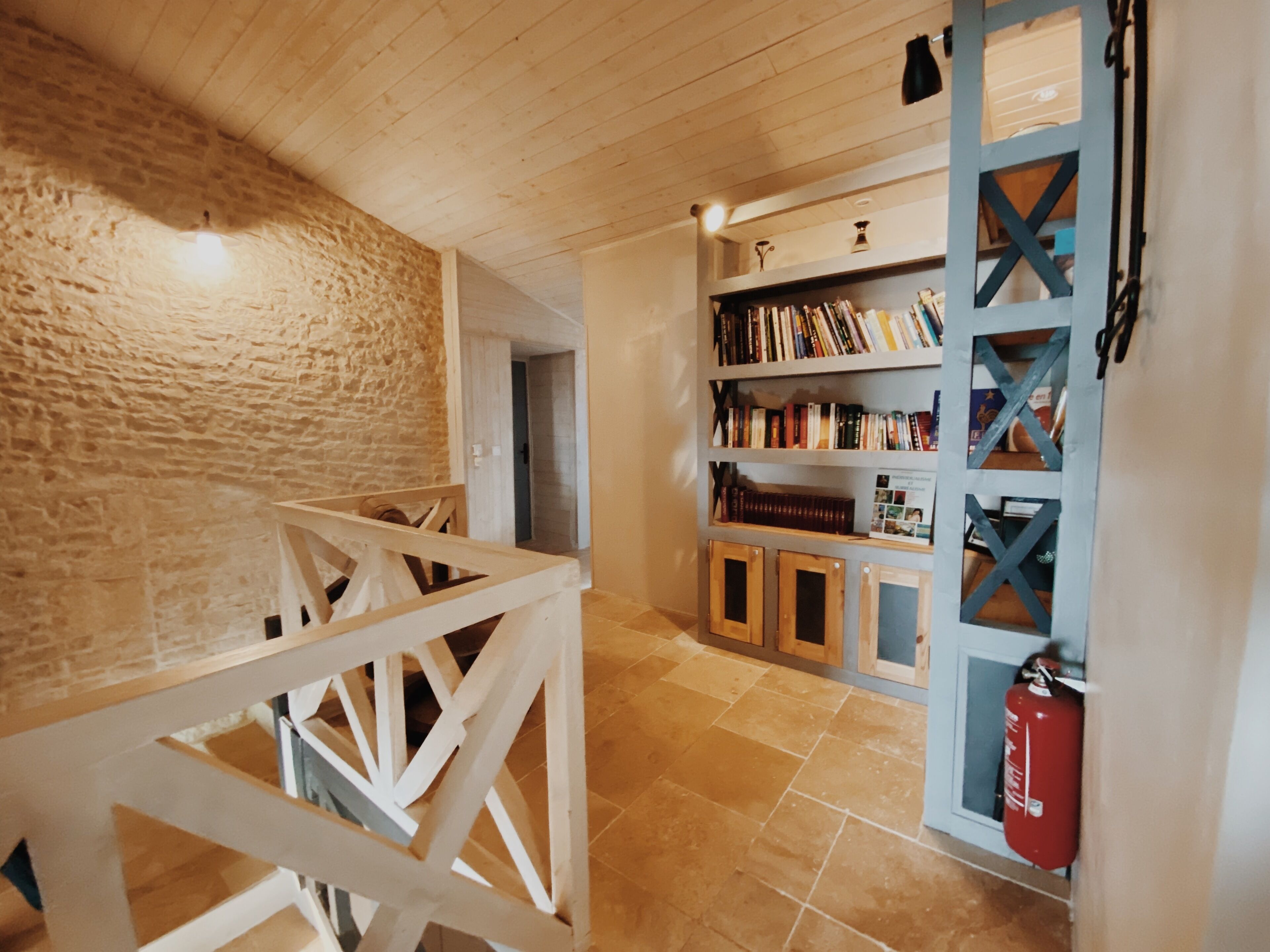 A wooden staircase leading to a room with a stone wall, a bookshelf, and a fire extinguisher.