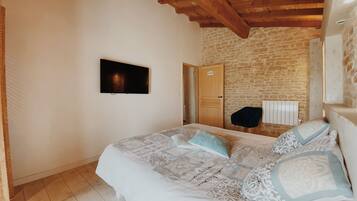 A bedroom with a bed, a television mounted on the wall, a wooden ceiling, and a stone wall.