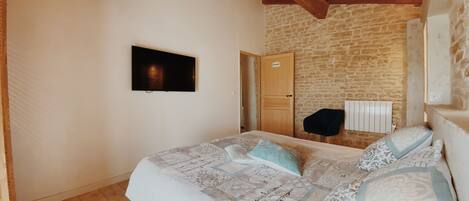 A bedroom with a bed, a television mounted on the wall, a wooden ceiling, and a stone wall.