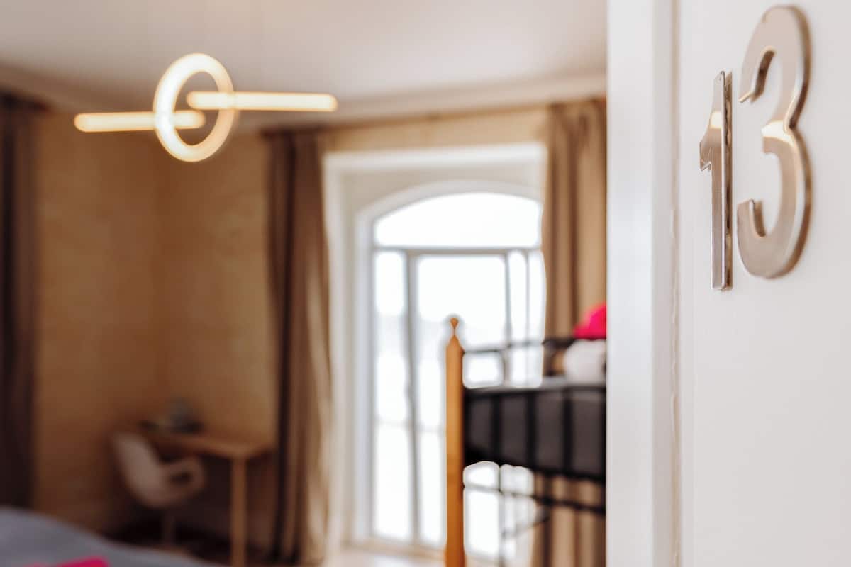 Une chambre avec un lit superposé, un bureau et une chaise. On peut voir le chiffre « 13 » sur le mur.