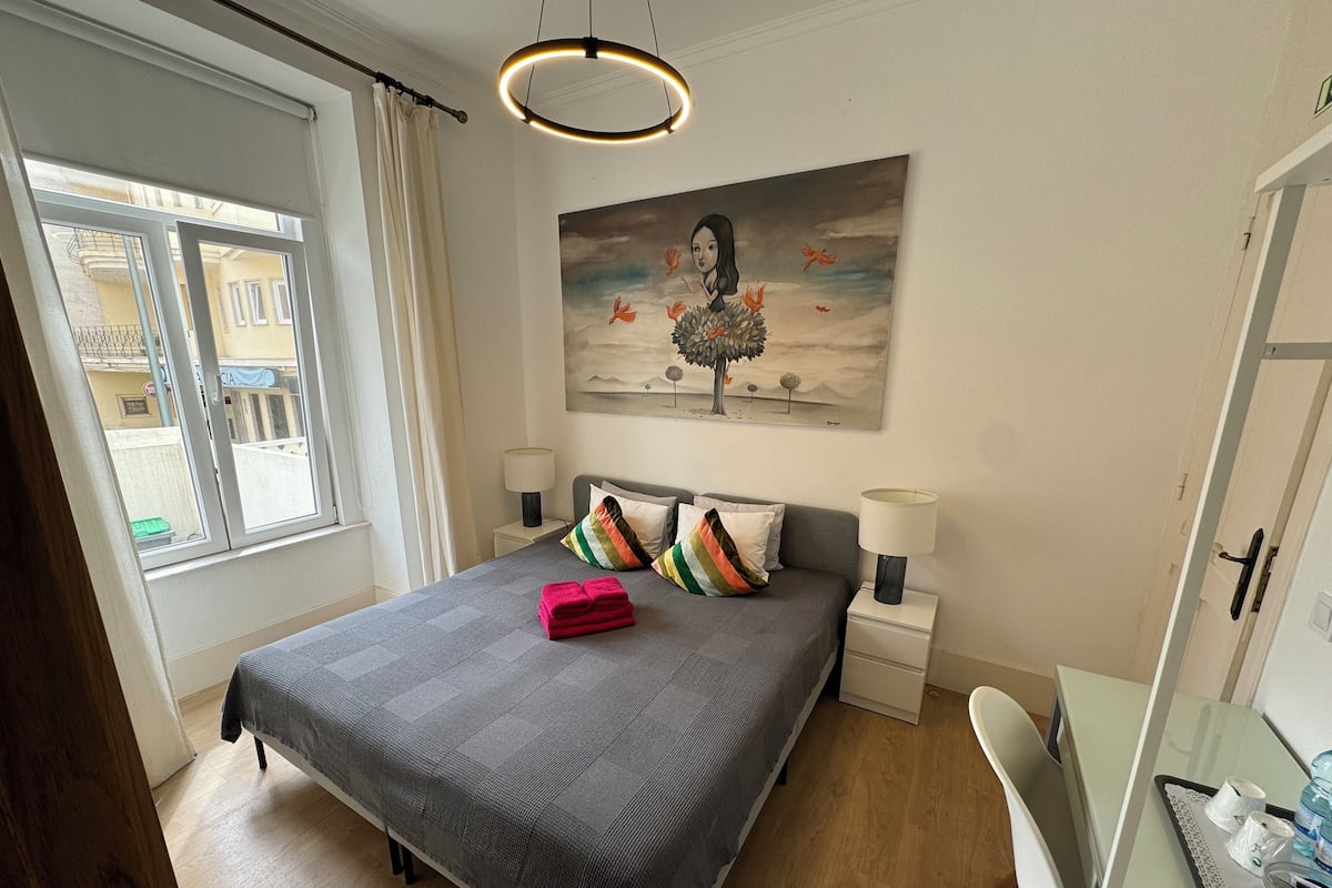 Une chambre à coucher avec un lit, deux tables de chevet, un bureau, une chaise et un tableau au mur.