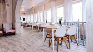 Une salle à manger spacieuse avec de hauts plafonds, de grandes fenêtres et un balcon doté d’une balustrade.