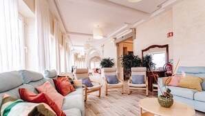 Un hall d’hôtel spacieux, doté d’un sol en bois de couleur claire, d’un grand canapé agrémenté de coussins colorés et de plusieurs fauteuils.