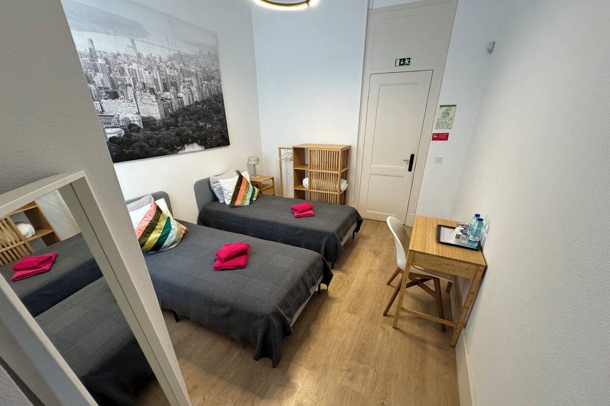 Une petite pièce propre, avec deux lits, un bureau et une chaise. Il y a une fenêtre donnant sur la ville et une porte avec un panneau indiquant la sortie de secours.