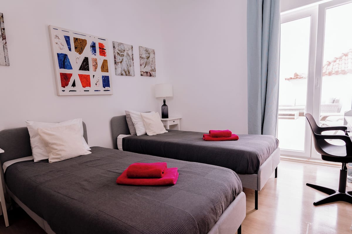 Une chambre d’hôtel avec deux lits, un bureau, une chaise et des œuvres d’art accrochées au mur.