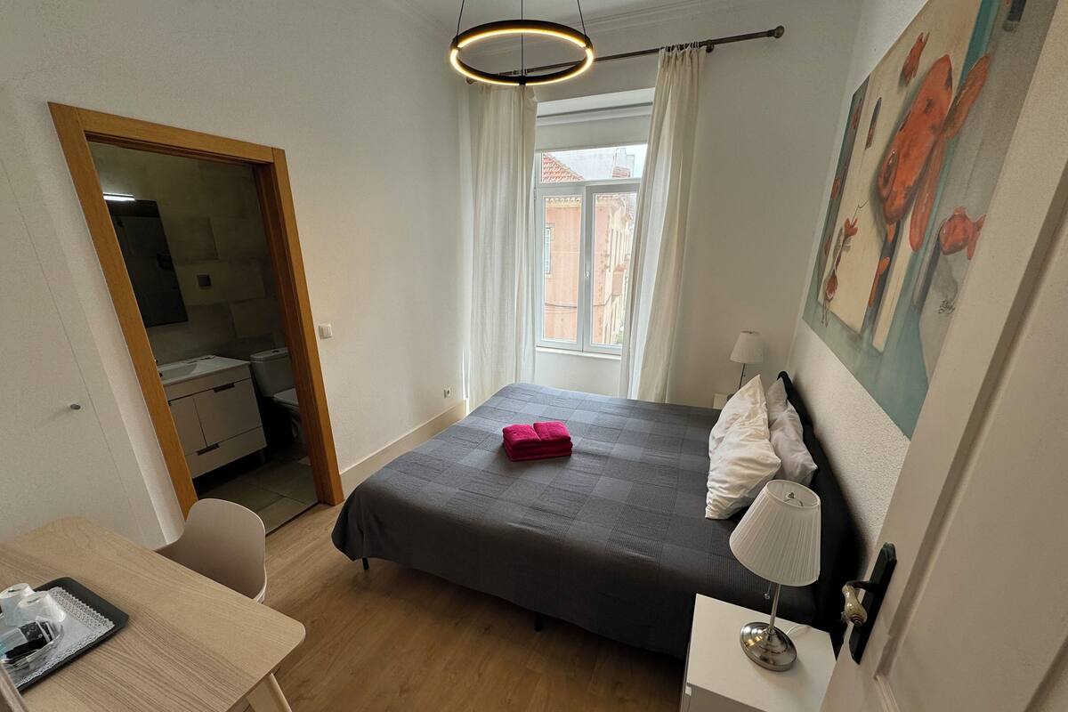 Une chambre à coucher avec un lit, un bureau, une chaise, une lampe et un tableau au mur.