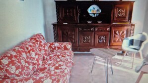 Un salon avec un canapé à motifs floraux, un meuble en bois orné d’objets décoratifs et une chaise blanche.