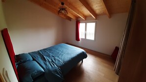 Une chambre à coucher avec un lit, des poutres en bois au plafond, une fenêtre avec des rideaux rouges et une porte.