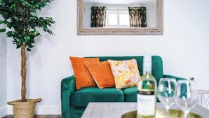 A green sofa with orange and multicolored pillows, a bottle of white wine, and two glasses on a tray. - Parkview Place by Patternbricks (Coventry)
